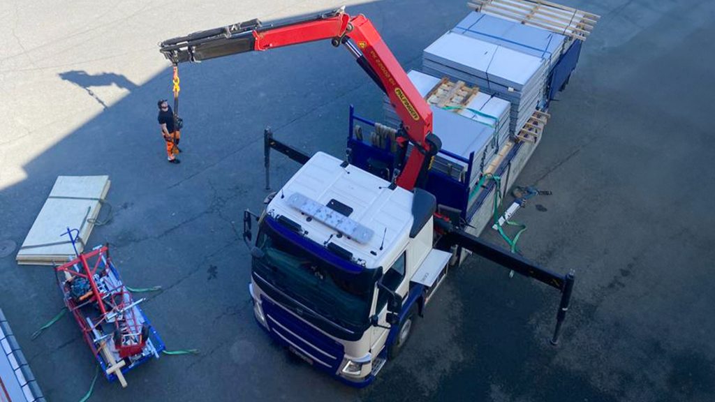 Savunpoistoluukkujen kansien vaihtoa. Nosturilla varustettu kuorma-auto nostamassa luukkujen kansia katolle. Luukkujen kannet ovat umpimallisia eli peltiverhoiltuja.