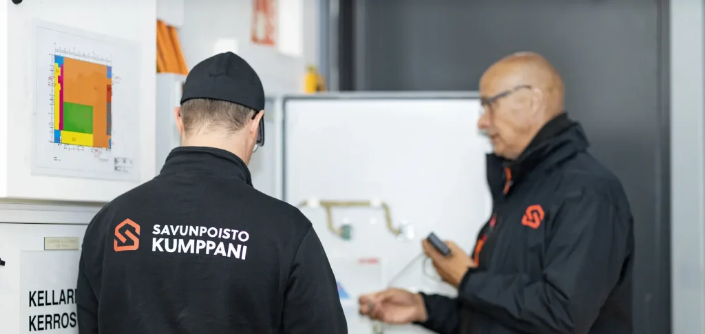 Kaksi Savunpoistokumppanin huoltoteknikkoa huoltamassa savunpoistokeskusta kiinteistössä.